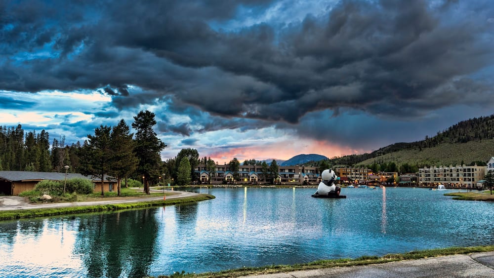 A lake with a boat, surrounded by buildings and trees under a cloudy sky.