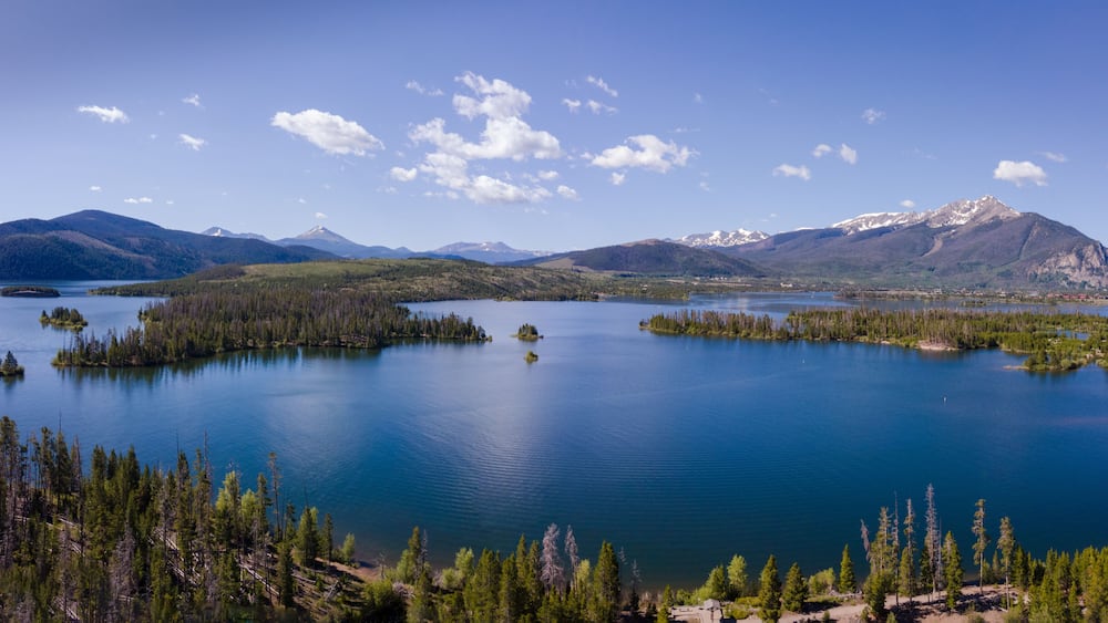 A large lake surrounded by dense forests and mountains with snow-capped peaks.