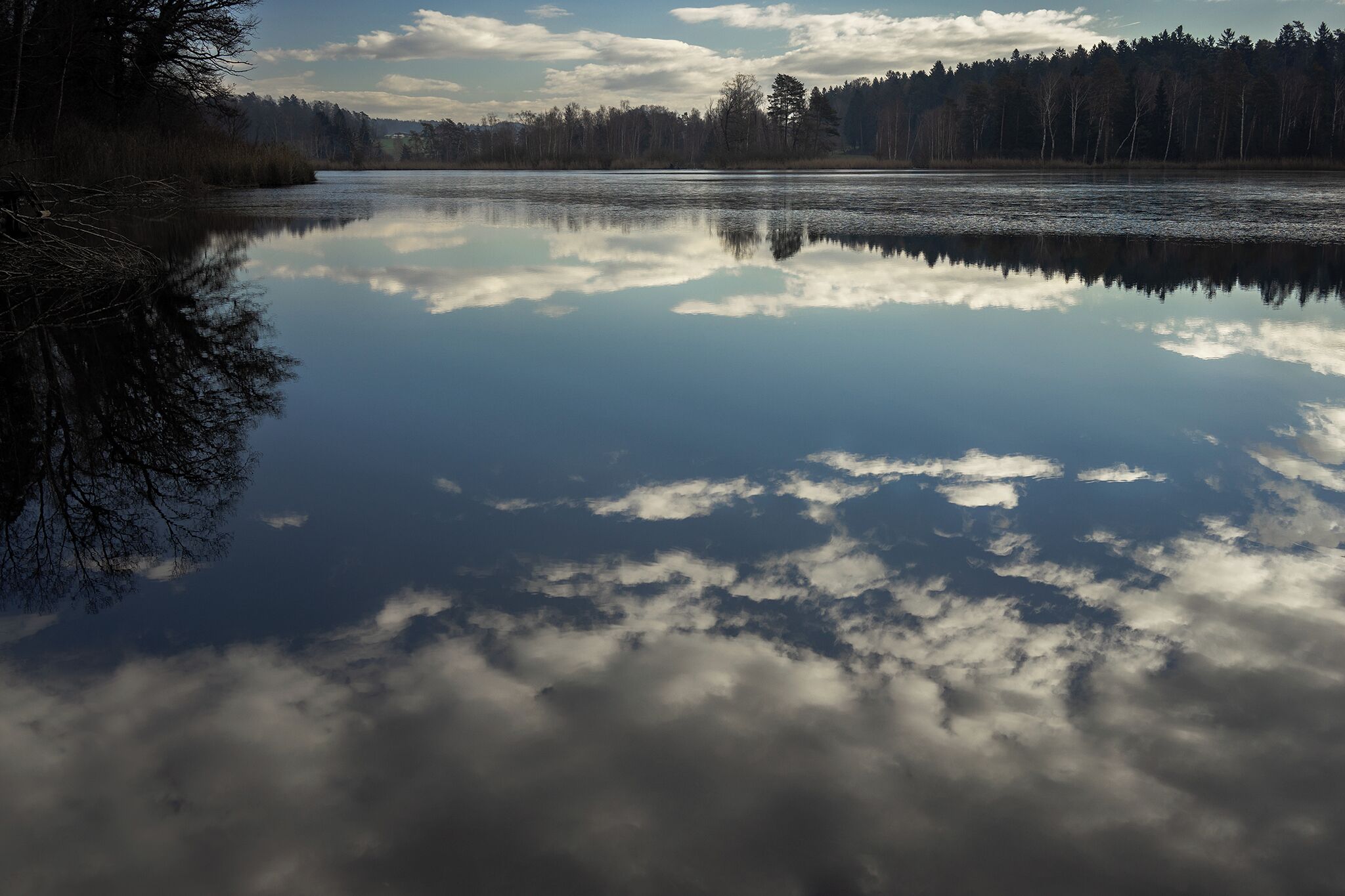 A calm lake reflecting trees and clouds.