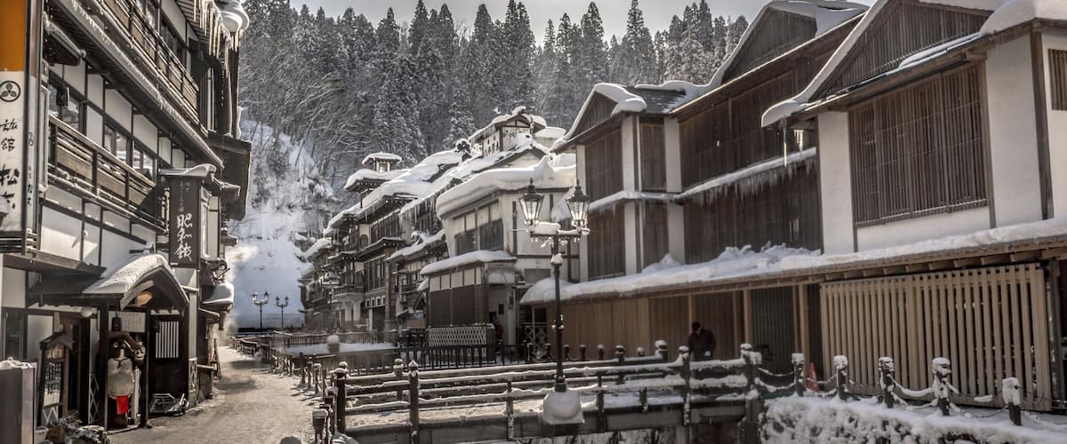 A snow-covered street with traditional buildings, a wooden bridge, and a river.