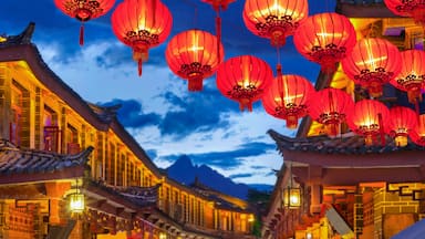 Una calle tradicional china al atardecer con faroles rojos, tejados ornamentados y una montaña de fondo.
