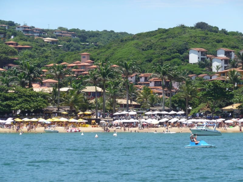 A beach with palm trees, umbrellas, and people.