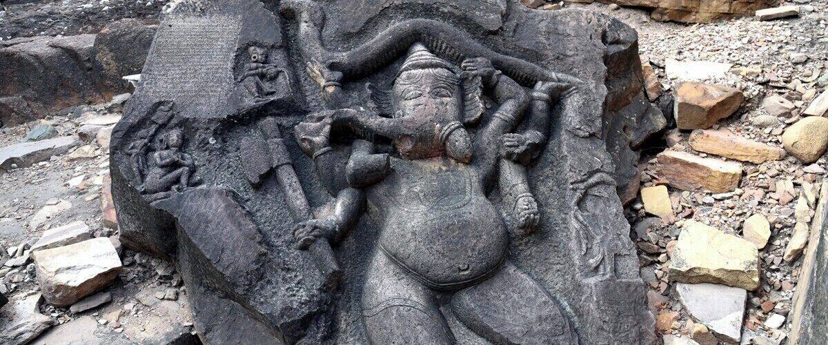A stone sculpture of a deity with multiple arms, surrounded by broken stone blocks.