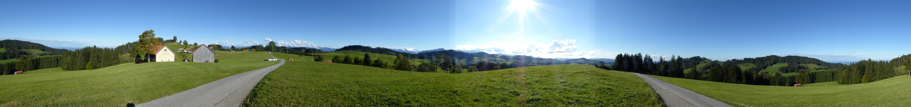 A rural landscape with a winding road, green fields, and distant mountains.