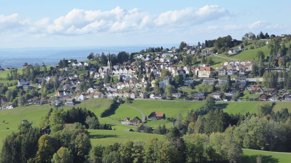 A picturesque village with rolling hills, a church, and a view of the sea.