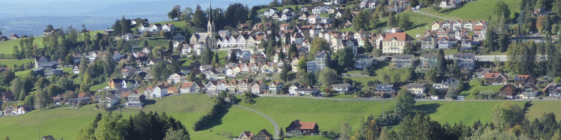 A picturesque village with rolling hills, a church, and a view of the sea.