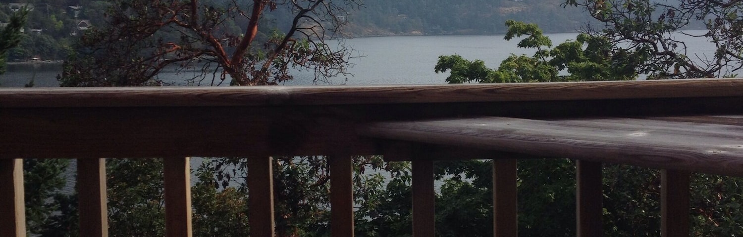 A wooden deck with a patterned pillow, overlooking a lake with mountains in the background.