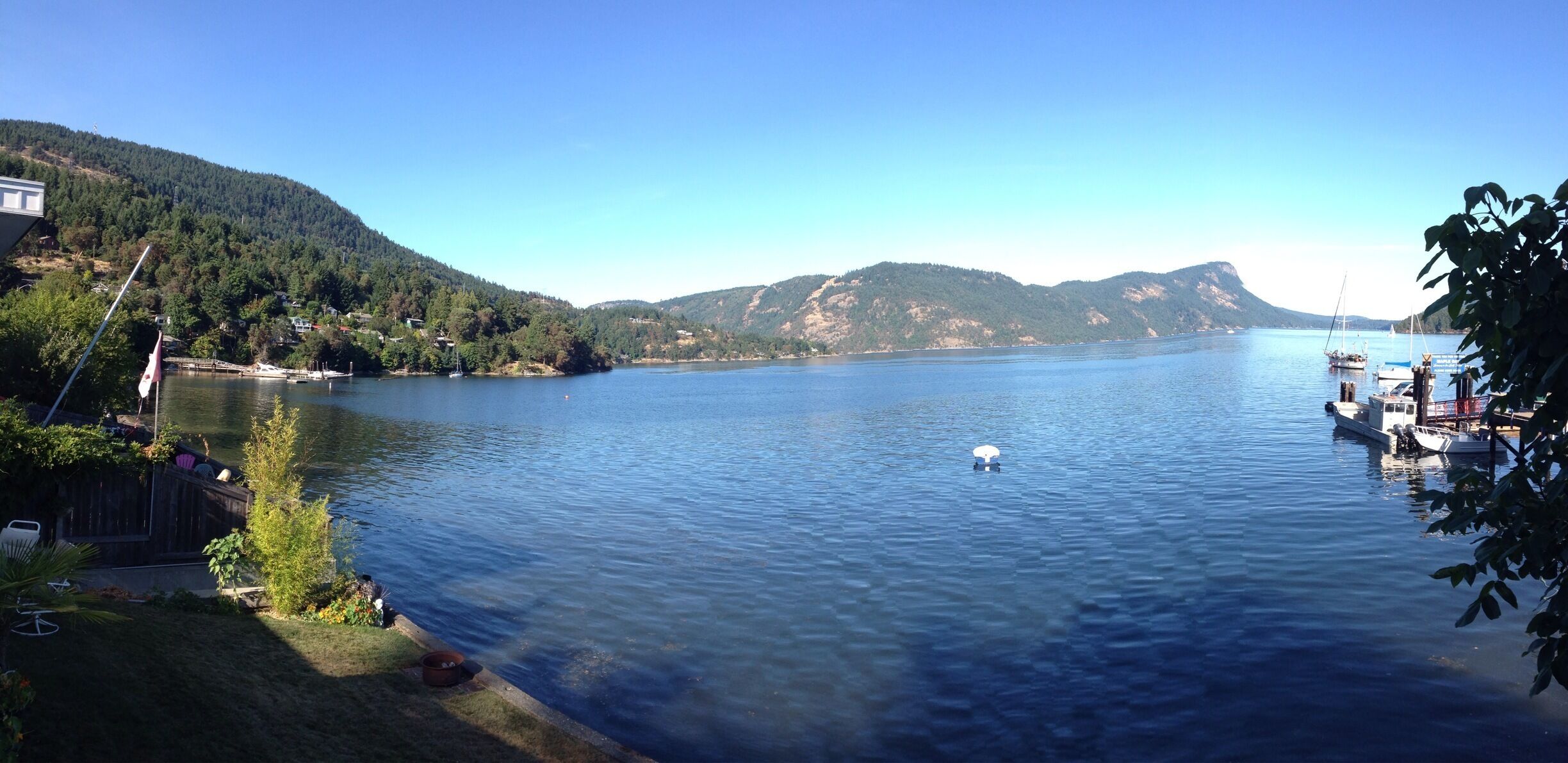 A calm lake surrounded by hills, boats docked at the shore, and a clear blue sky.