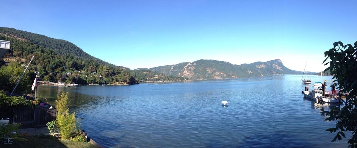 A calm lake surrounded by hills, boats docked at the shore, and a clear blue sky.