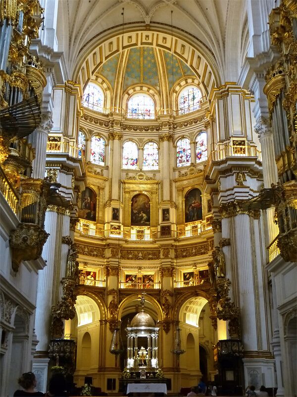 An ornate church interior with gold accents, stained glass windows, and a central altar.