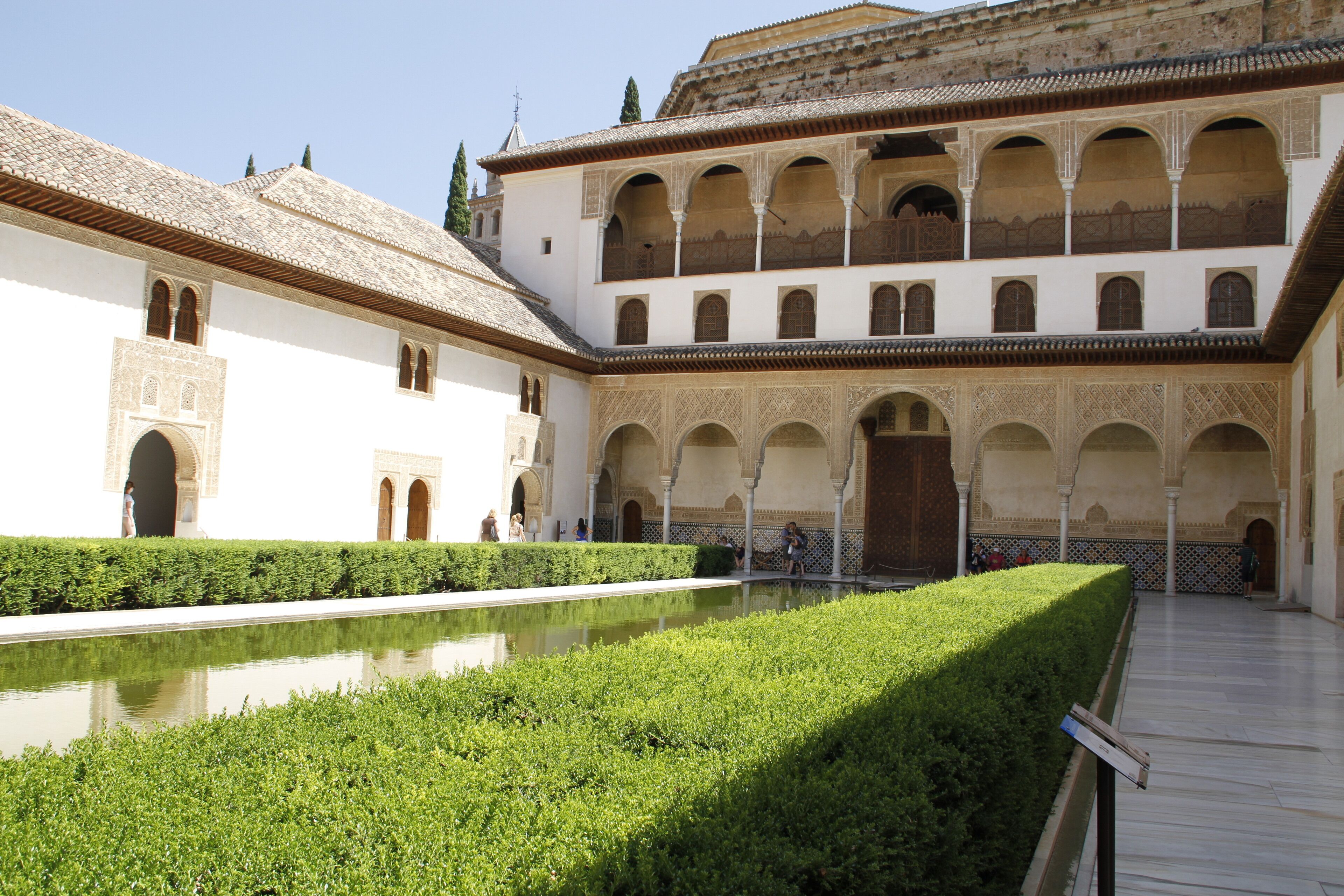 Un patio con piscina, paredes blancas, arcos y techo de tejas.