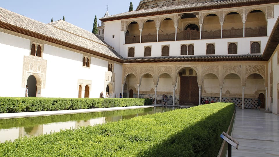 Un patio con piscina, paredes blancas, arcos y techo de tejas.