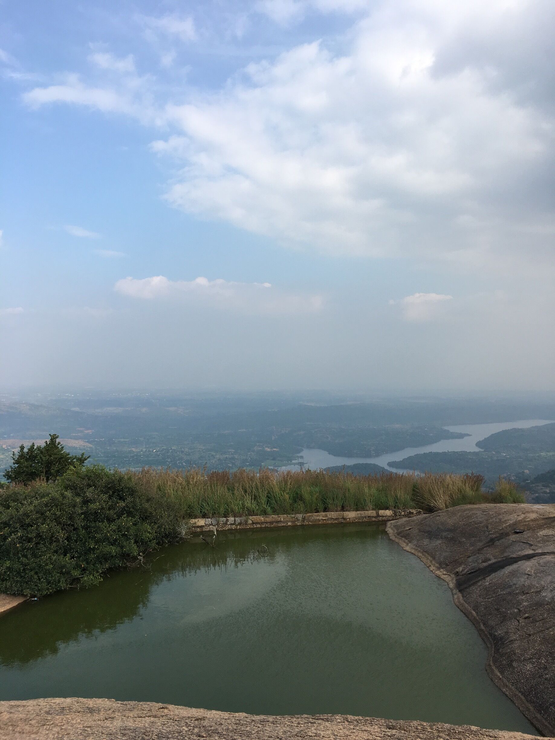 A panoramic view of a lake surrounded by hills and a distant cityscape.