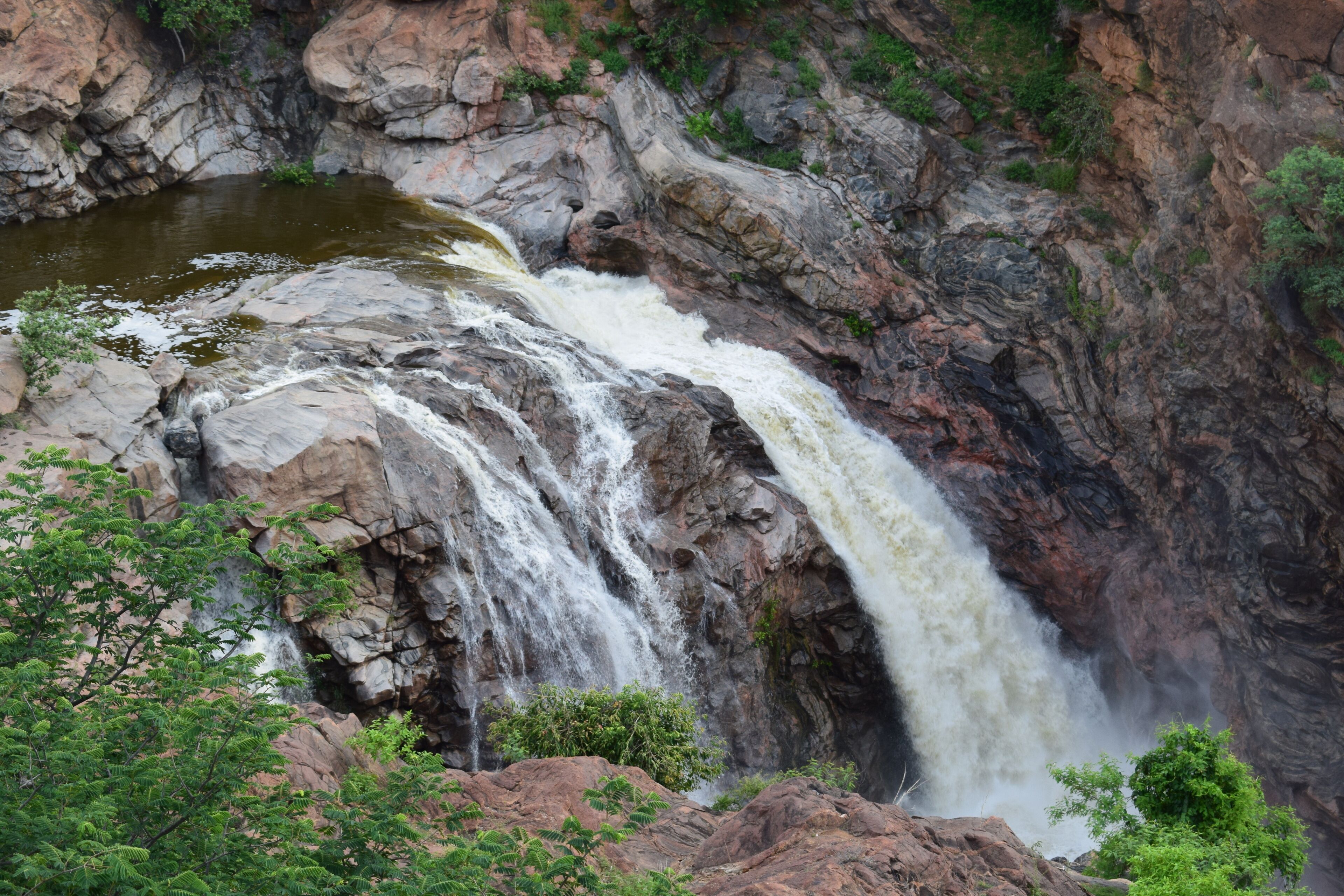 A waterfall cascading down a rocky cliff surrounded by greenery.