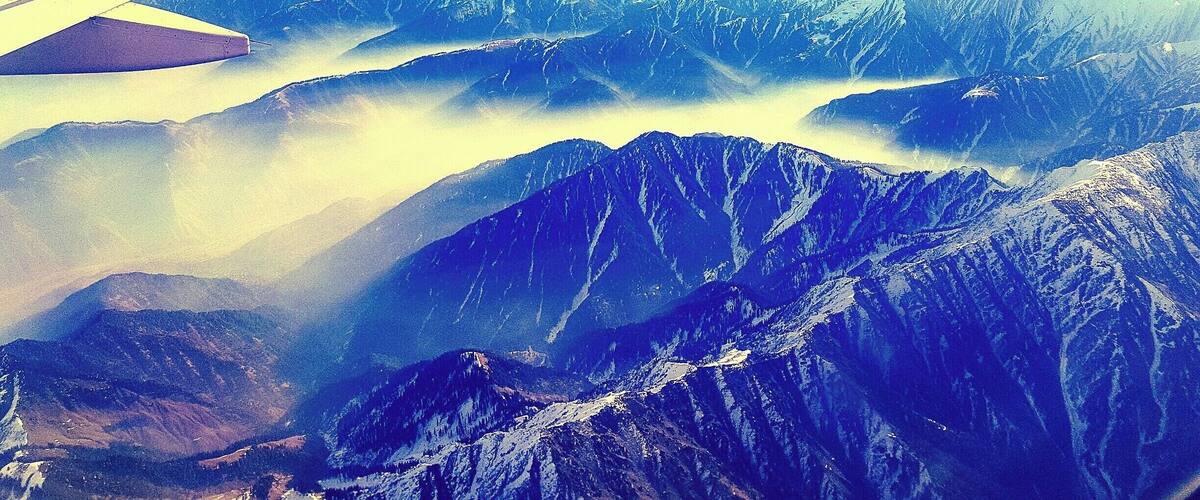 An airplane wing with a purple tip flying over snow-covered mountains and valleys.
