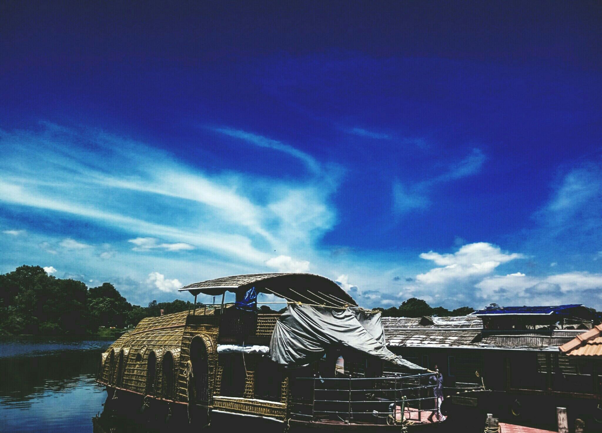A traditional boat with a thatched roof, docked at a calm river.