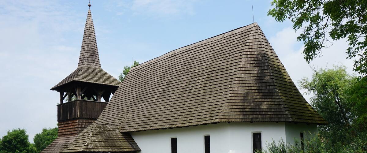 A traditional wooden church with a conical roof and a bell tower.