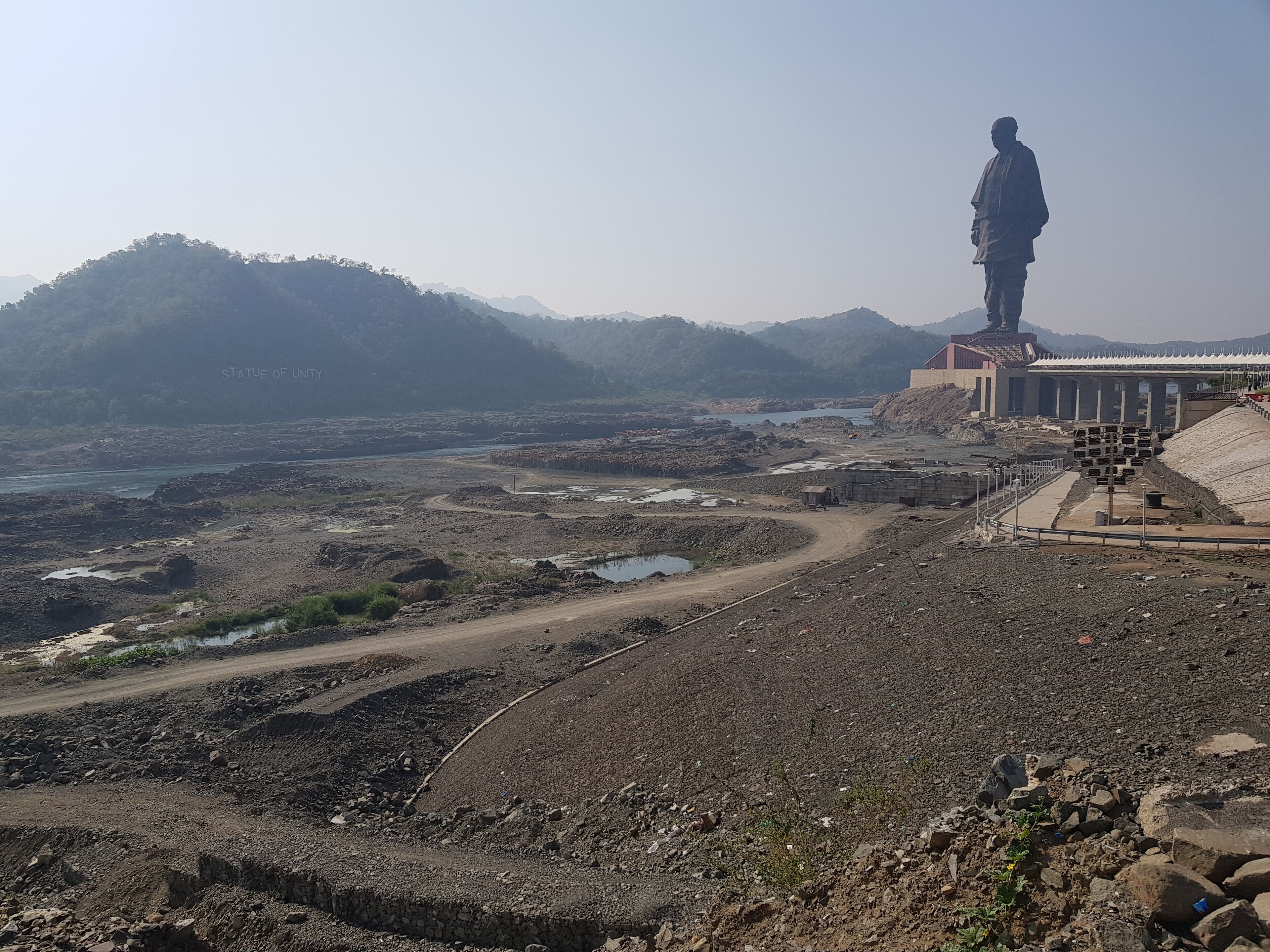 A statue on a hill overlooking a river and a construction site.