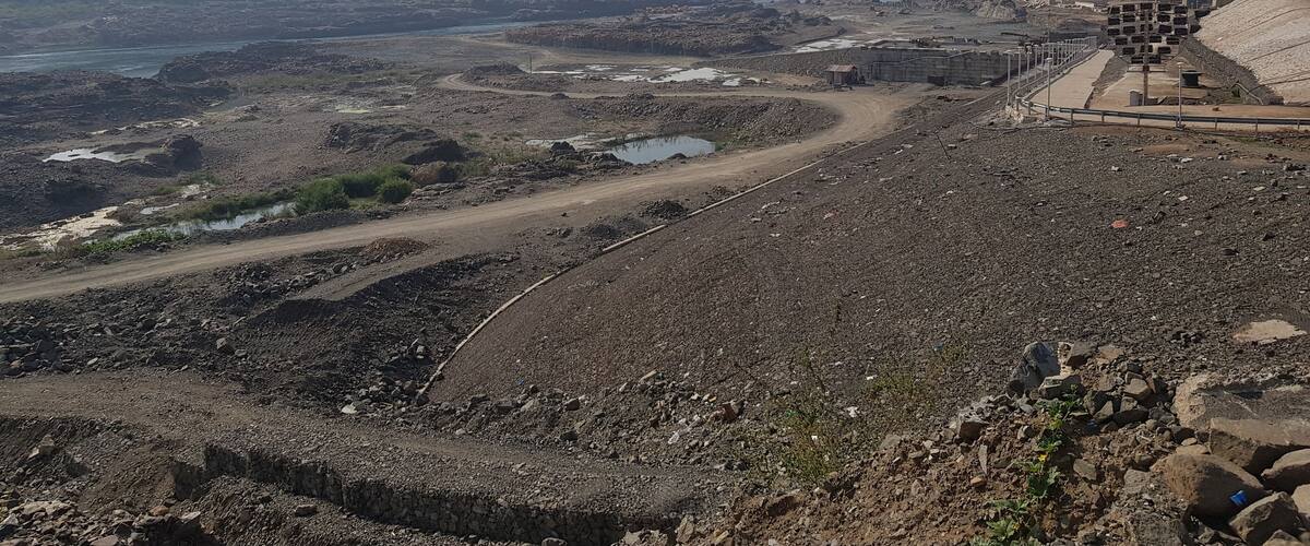 A statue on a hill overlooking a river and a construction site.