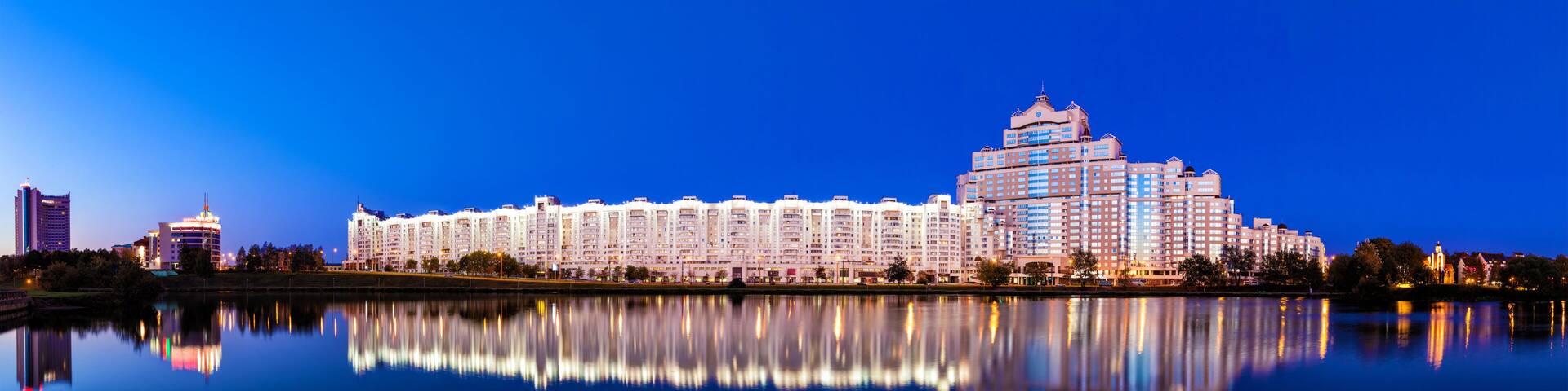 A waterfront cityscape with a large hotel and other buildings reflected in calm water.