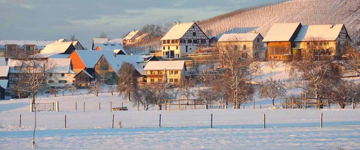 Un pueblo cubierto de nieve con casas tradicionales de entramado y una colina al fondo.