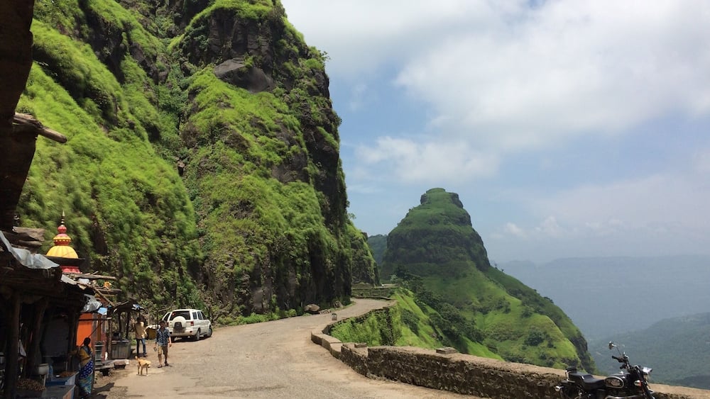 A mountainous landscape with a winding road, a yellow temple, and a parked motorcycle.