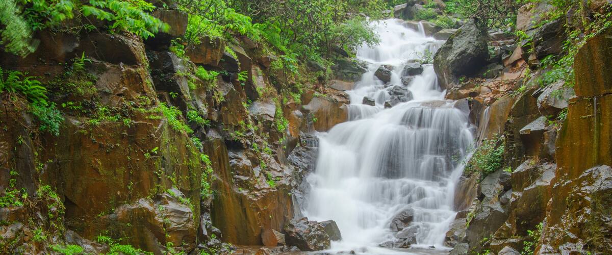 A multi-tiered waterfall surrounded by rocky cliffs and lush greenery.