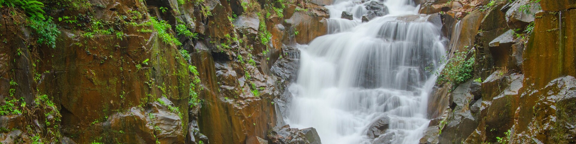 A multi-tiered waterfall surrounded by rocky cliffs and lush greenery.