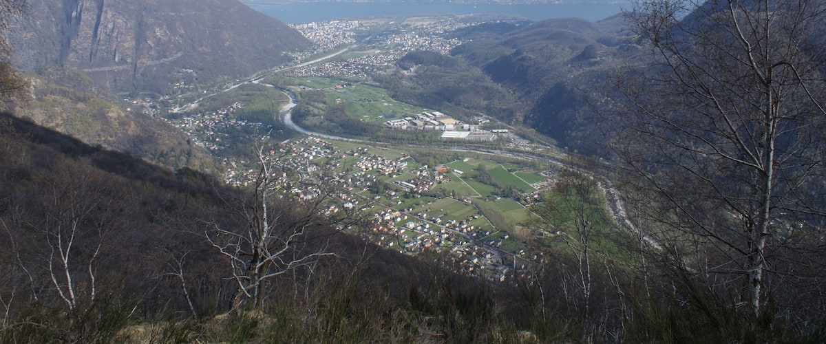 A mountainous landscape with a valley, a river, and snow-capped mountains in the background.