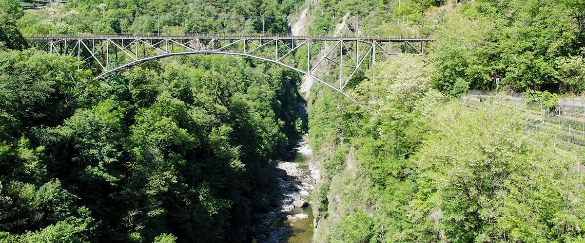 Eine Stahlbrücke überspannt ein Tal mit bewaldeten Hängen.