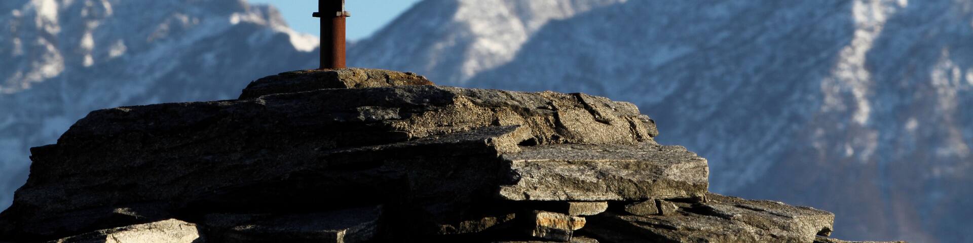 Cross over the slate roof of a chapel at Comoi, Tegna. In the background the Lugano Prealps.
