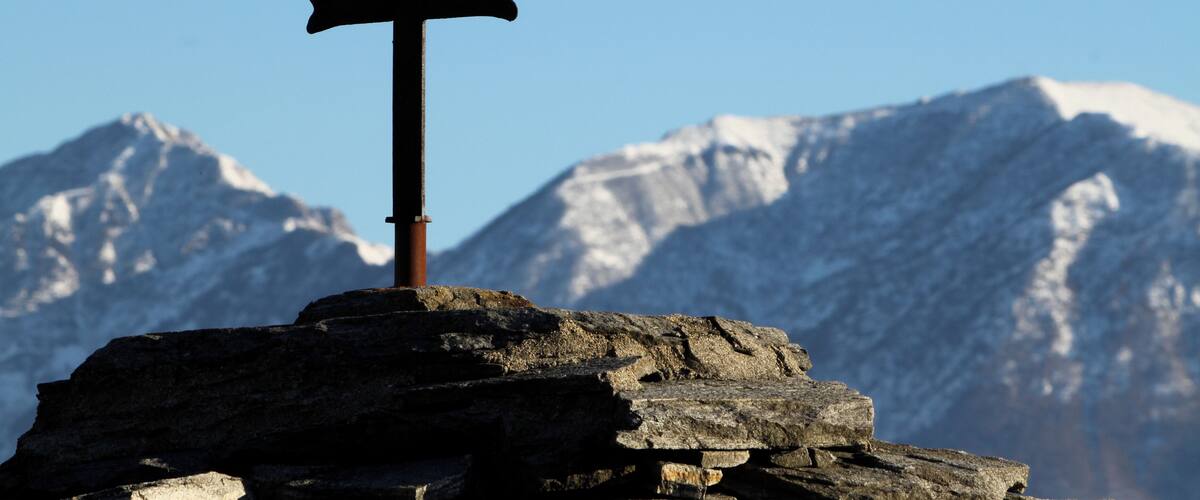 A cross on a rock with snow-capped mountains in the background.