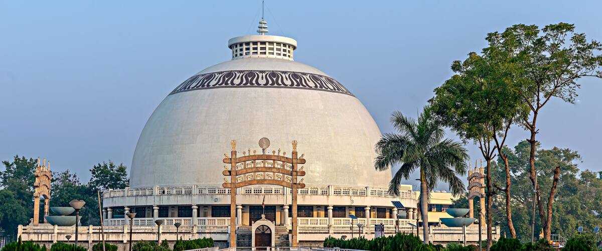 A large domed building with a central entrance, surrounded by a white fence and palm trees.