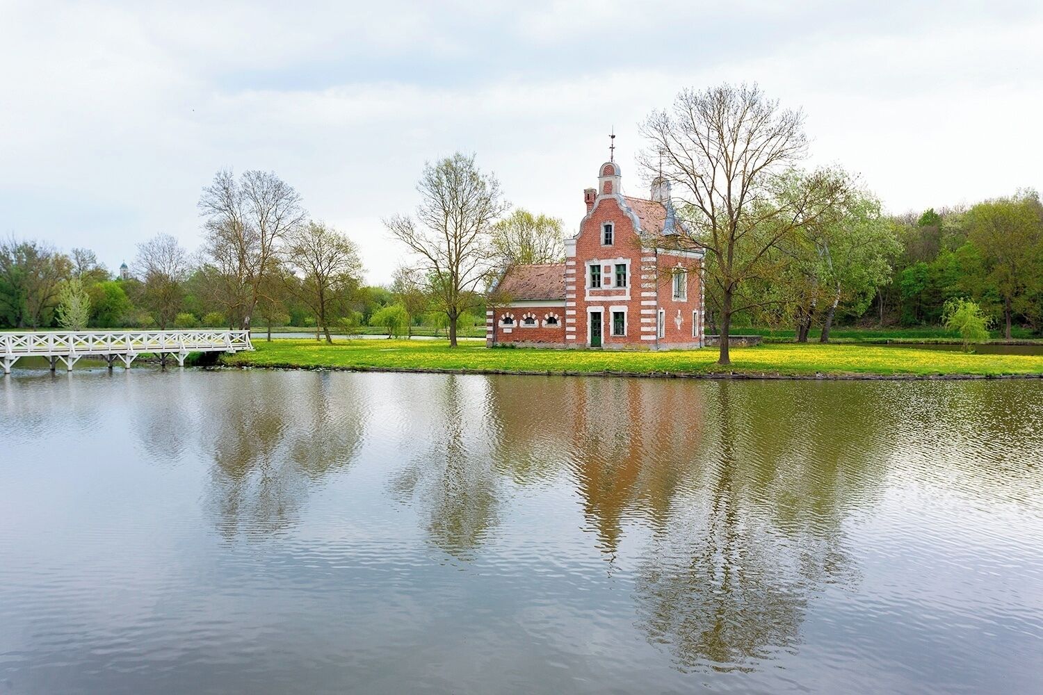 A brick house with a tower, a bridge, and a calm lake.