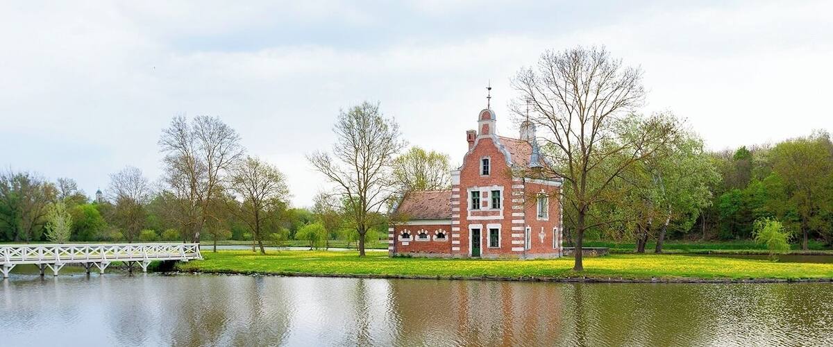A brick house with a tower, a bridge, and a calm lake.