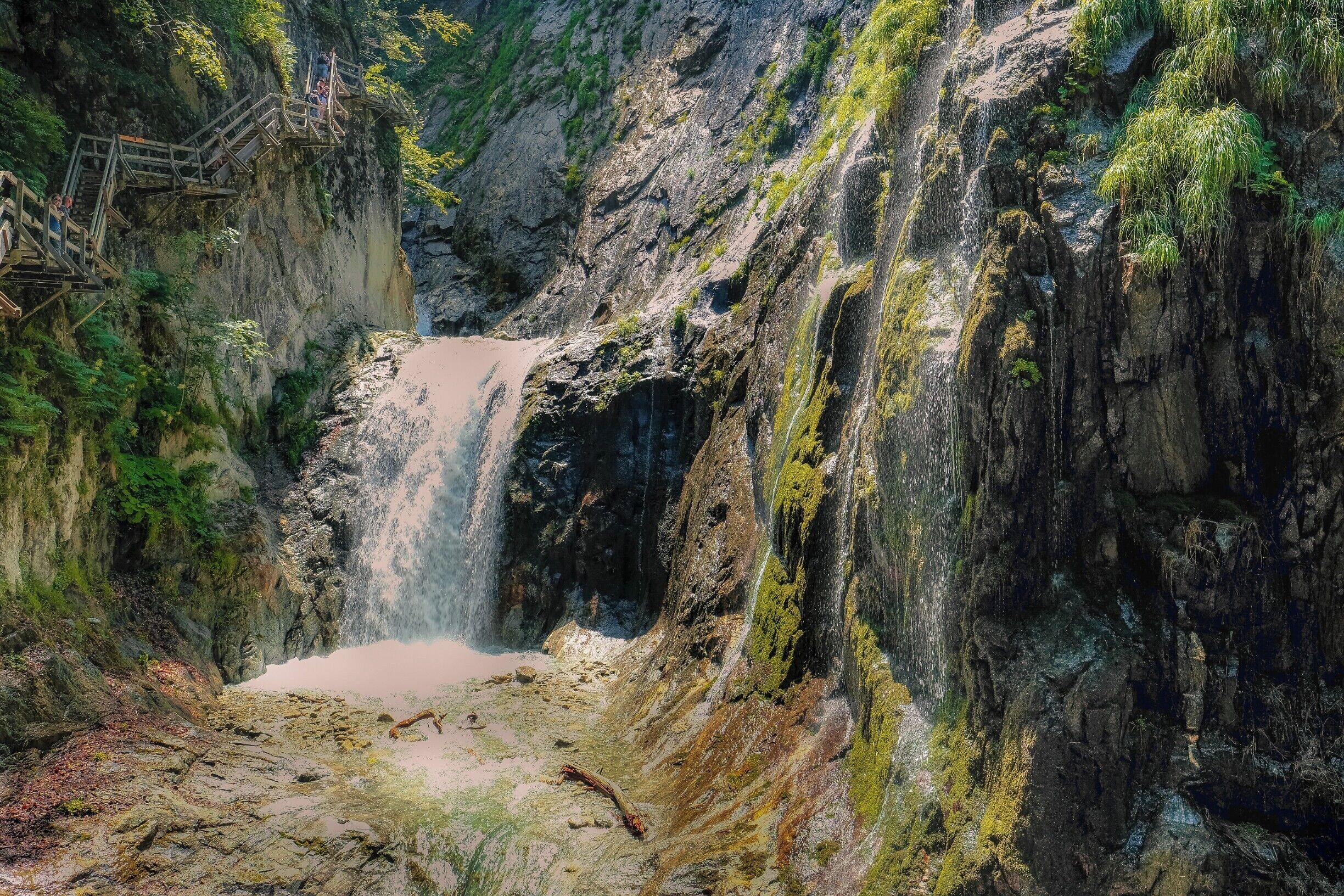 A waterfall cascading down a rocky cliff with a wooden staircase on the left.