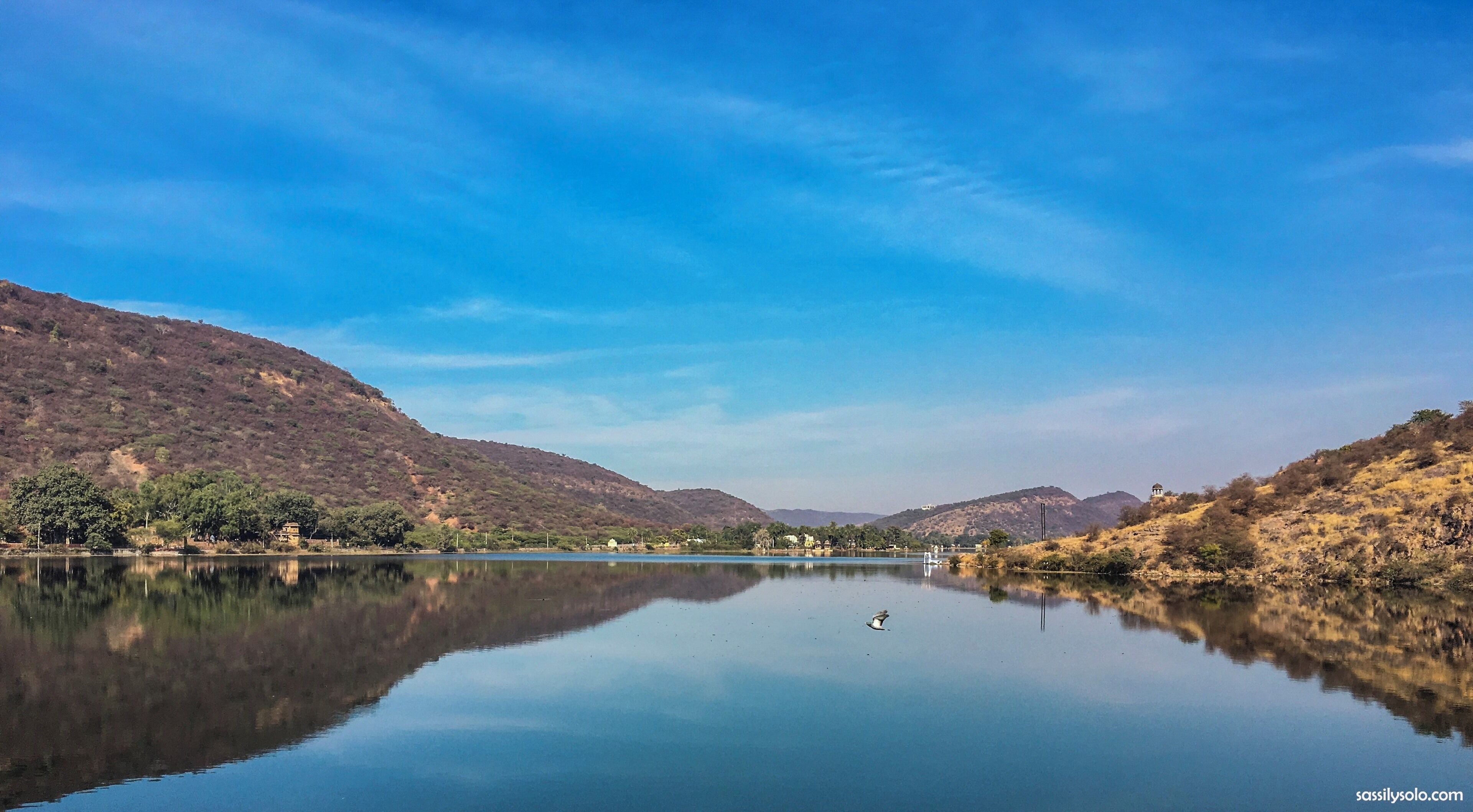 A calm lake with reflections of the surrounding hills and a clear blue sky.