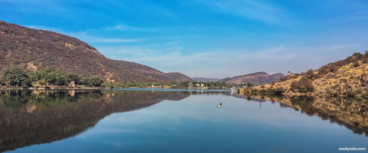 A calm lake with reflections of the surrounding hills and a clear blue sky.