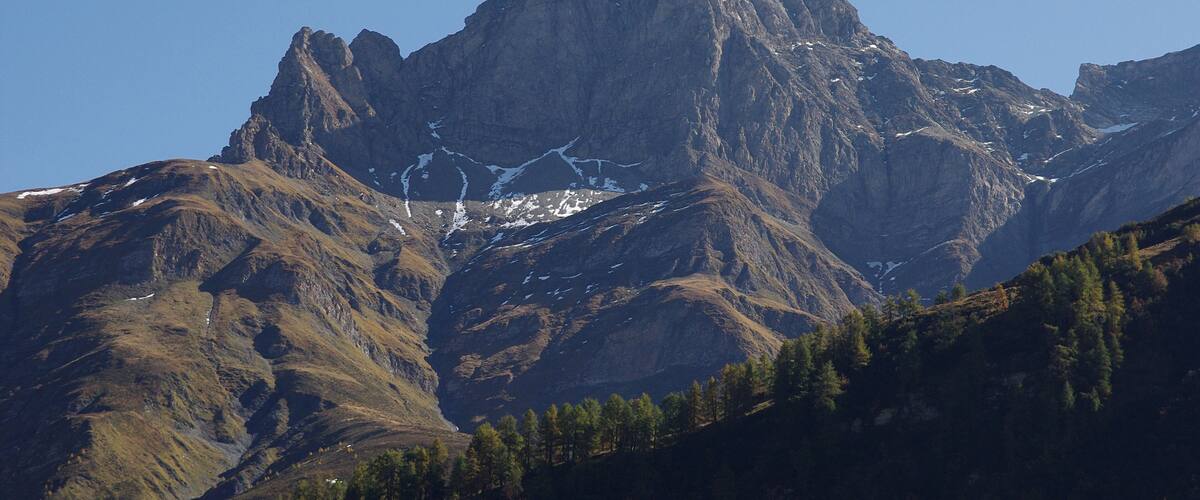 A rugged mountain peak with snow patches and a forested valley.