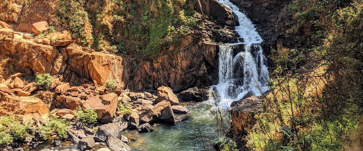 A waterfall cascading down a rocky cliff into a river surrounded by dense forest.