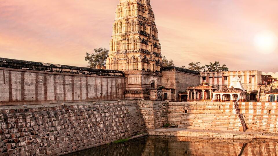 A temple with intricate carvings, a reflection in the water, and a sunset sky.