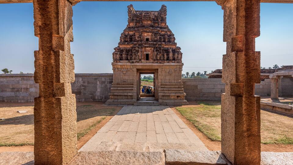 An ancient stone structure with intricate carvings, a paved pathway leading to it, and a clear blue sky in the background.