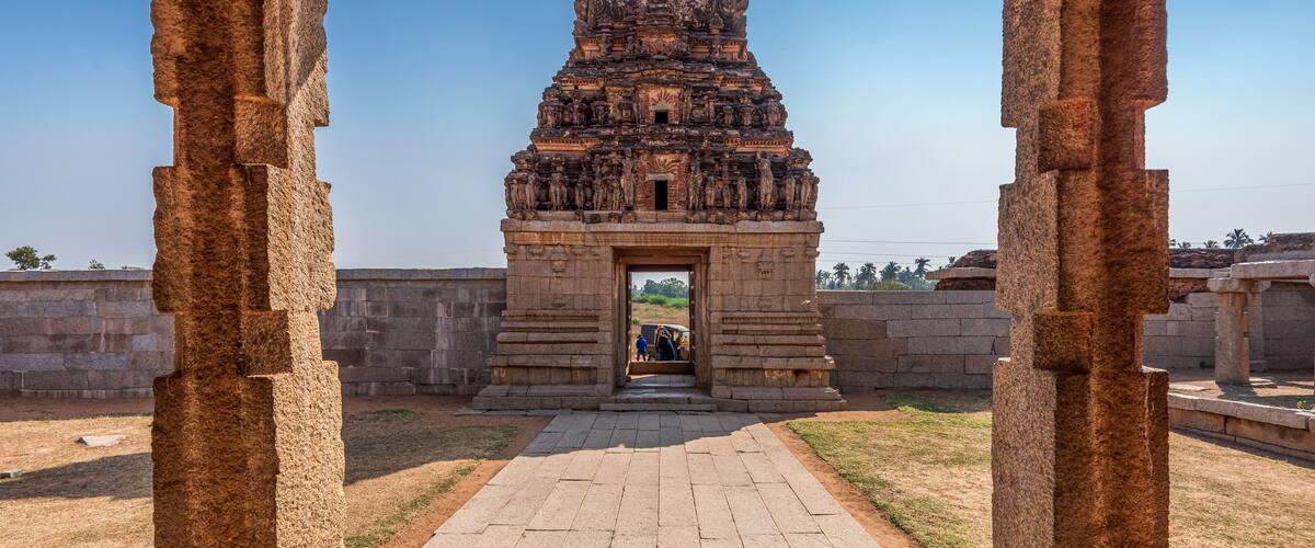 An ancient stone structure with intricate carvings, a paved pathway leading to it, and a clear blue sky in the background.