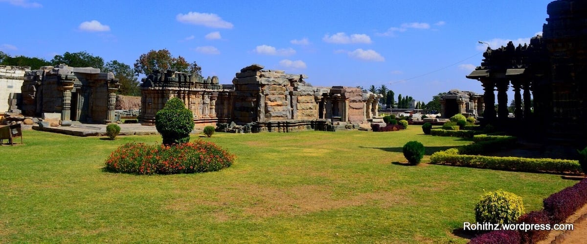 Ancient stone ruins with intricate carvings, surrounded by well-maintained lawns and flowering plants.