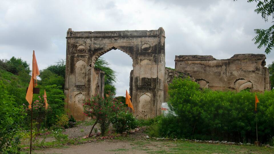 An ancient stone archway surrounded by lush greenery and orange flags.