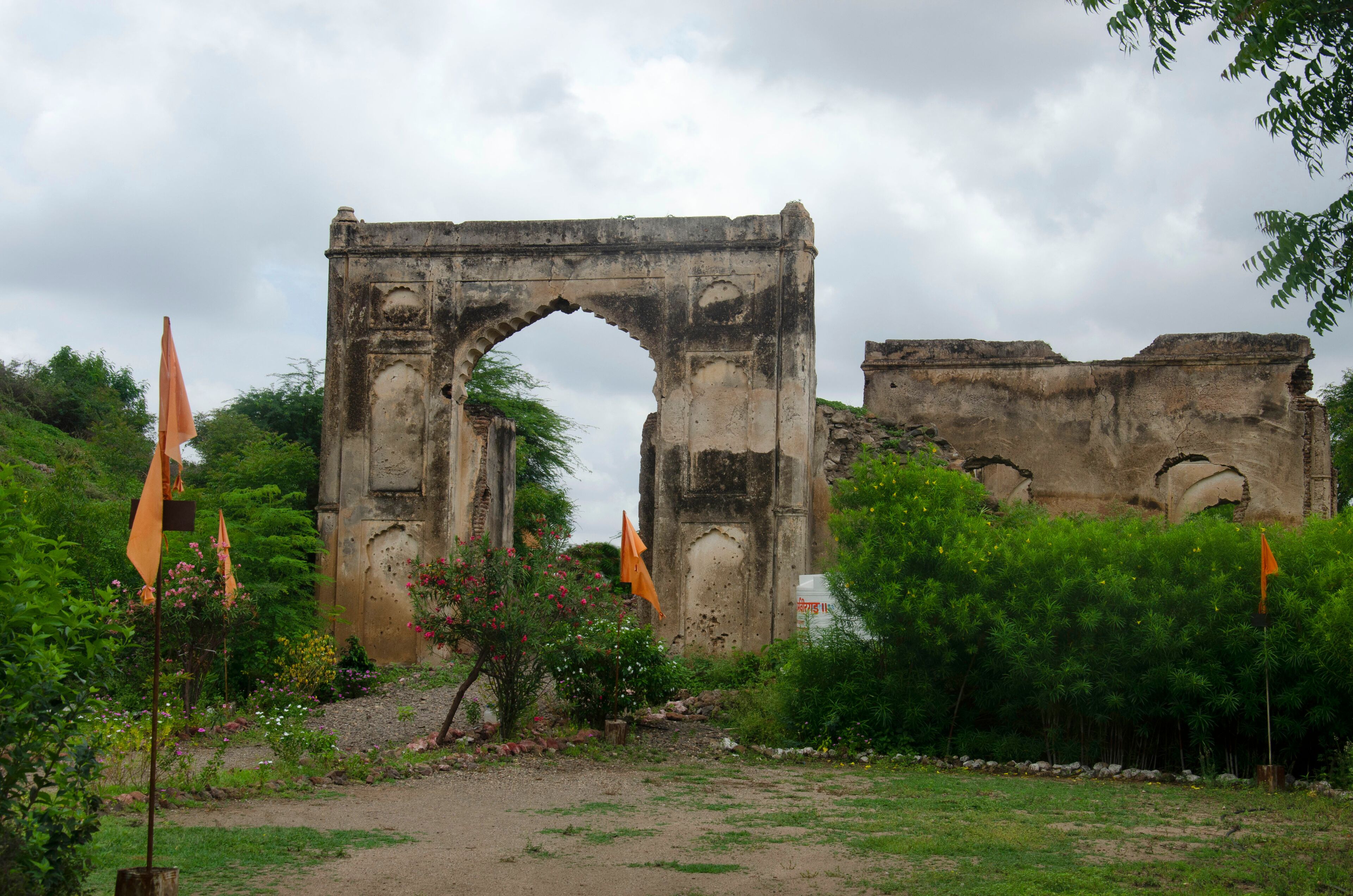 An ancient stone archway surrounded by lush greenery and orange flags.