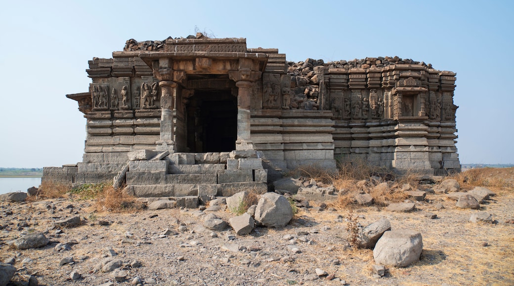 An ancient stone structure with intricate carvings, situated on a rocky terrain with sparse vegetation.