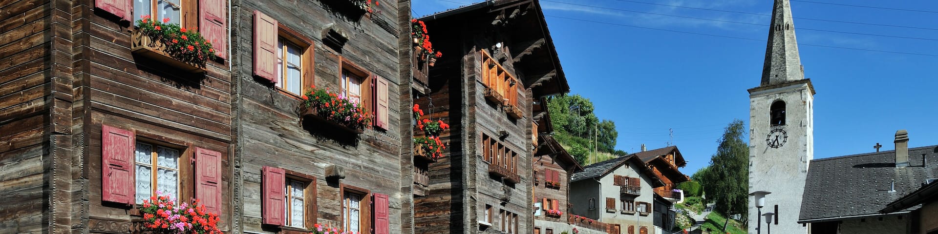BGPE8P Church and traditional wooden houses / chalets decorated with geraniums in the Alpine village Saint-Martin, Valais, Switzerland