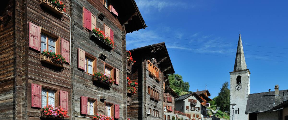 A charming European village with wooden buildings, flower boxes, and a church tower.
