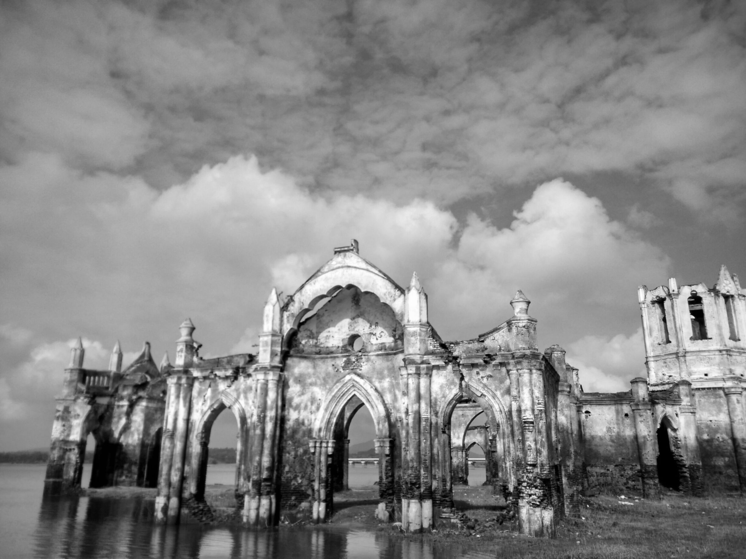An abandoned, dilapidated building with Gothic architecture, including pointed arches and a central dome, surrounded by water.